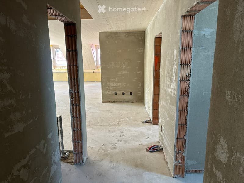 Unfurnished Room. Empty hallway with unfinished concrete walls and floor, exposed pipes, and construction materials visible.