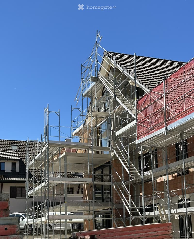 Building. A modern house under construction with scaffolding, exposed steel framework, and partially completed roofing.