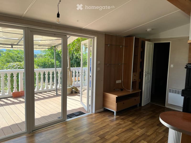 Bright room with wooden flooring, large sliding glass doors opening to a balcony with a view, a small table, a cabinet, and a radiator.