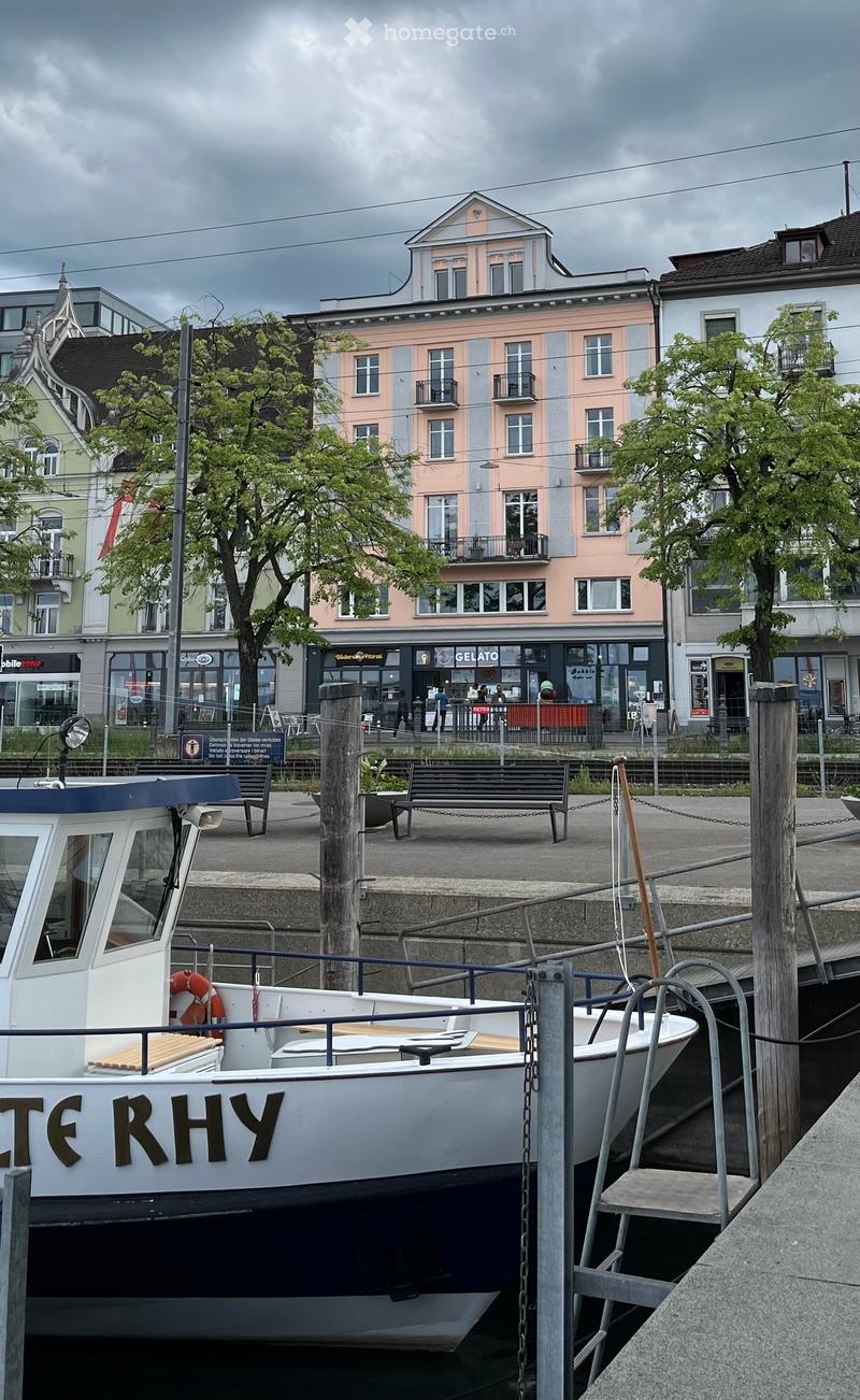 Garden / Outdoor Area. A boat named "TE RHY" is docked at a pier with a bench nearby, surrounded by urban buildings and trees.