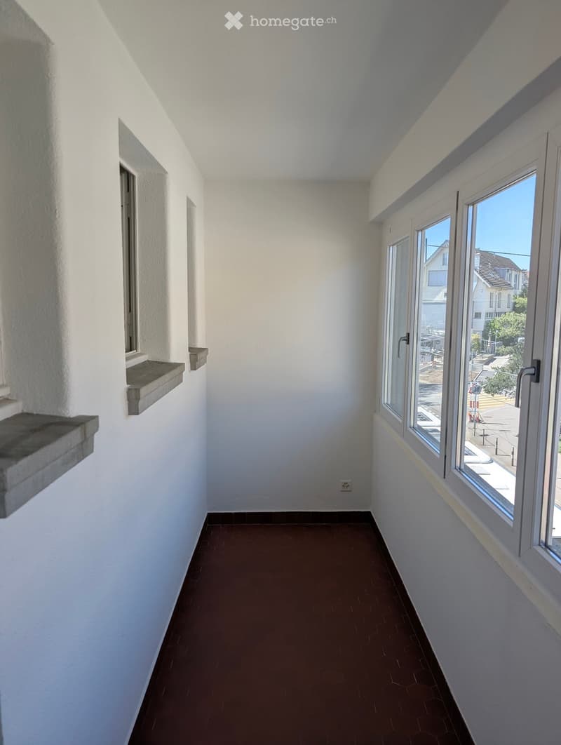 Empty room with white walls, brown floor, three windows, power outlet