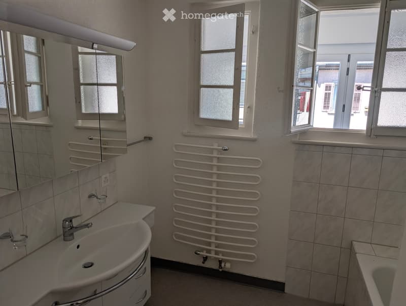 Bathroom with white tiles, white sink, mirror, bathtub, and a window.