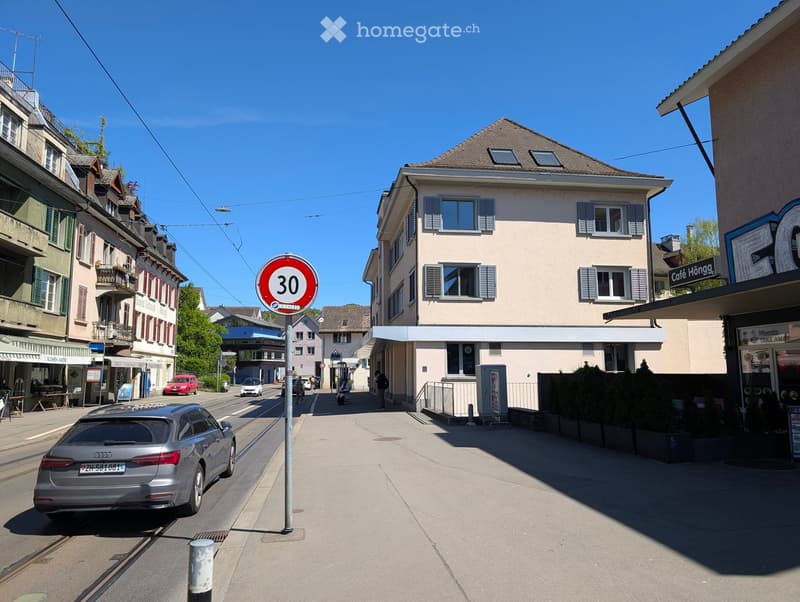 Urban street with a speed limit sign, buildings, parked cars, and pedestrians.