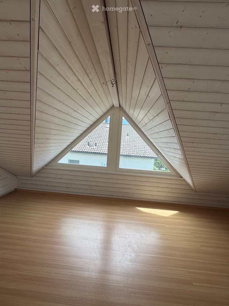 Unfurnished Room. Empty room with wooden floor and slanted wooden ceiling, featuring two triangular windows allowing natural light to enter.