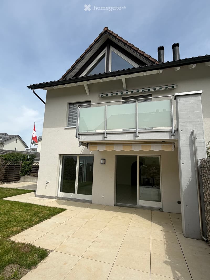 House. Two-story house with a modern design, featuring a balcony with glass railings, large windows, and a covered entrance area.