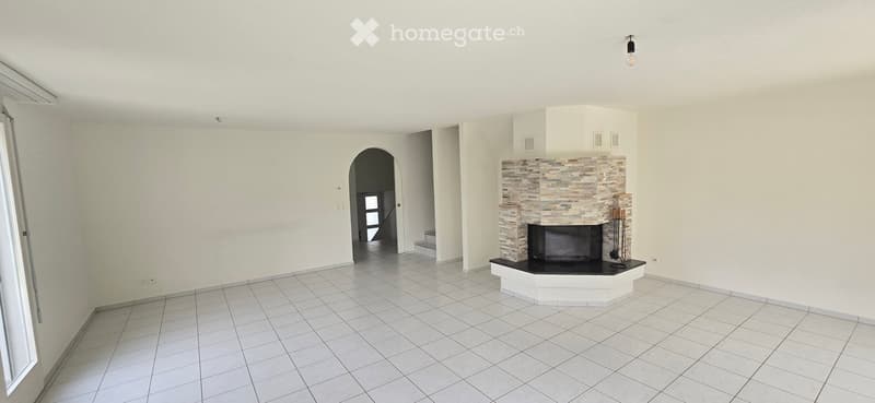 Unfurnished Room. Empty living room with white tiled flooring, white walls, and a stone fireplace with a black insert. An arched doorway leads to another room.