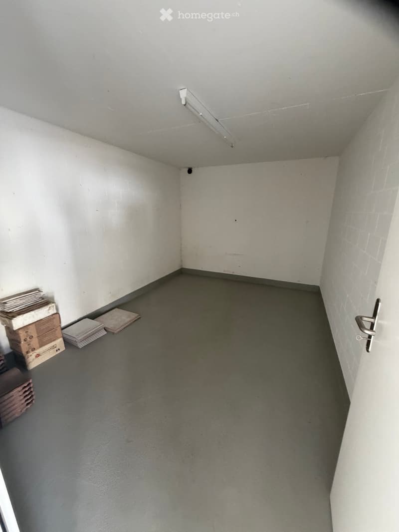 Unfurnished Room. Empty room with grey concrete floor and white walls, featuring a door on the right side and a stack of boxes and papers on the left side.