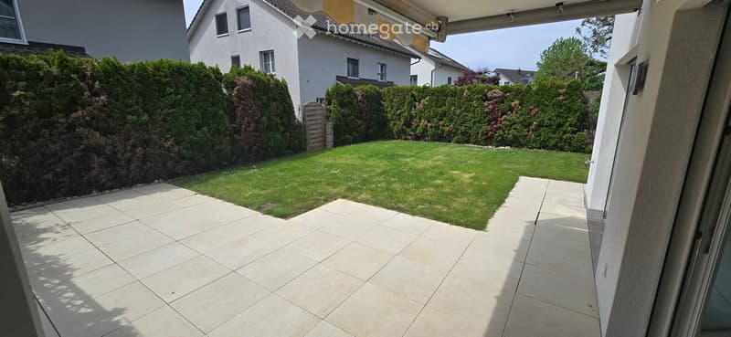Garden / Outdoor Area. Well-maintained garden with a neatly trimmed lawn, surrounded by tall hedges and treesE trees. The area features a tiled patio extending from the house.