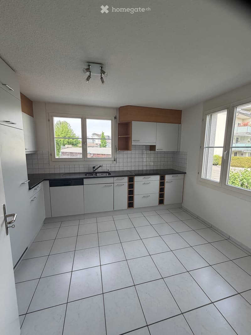 Unfurnished Room. Empty kitchen with white tiled floor, white cabinets, and a sink. Windows provide natural light, and the space is clean and uncluttered.