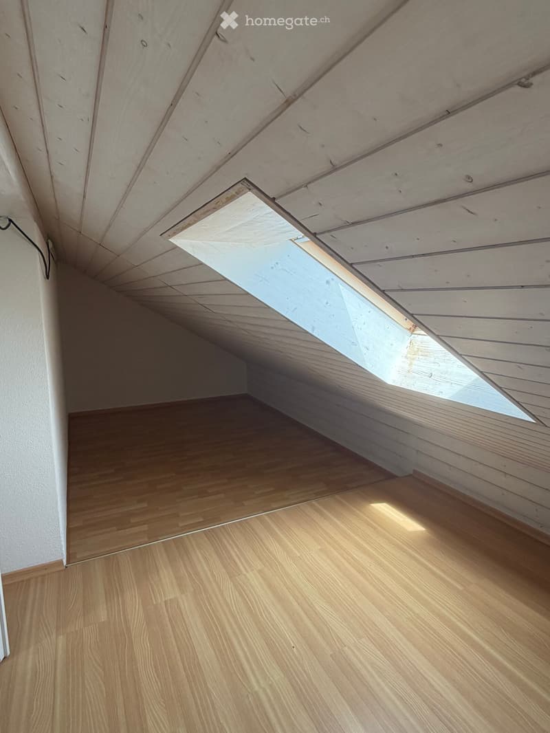 Unfurnished Room. Empty attic space with wooden flooring and exposed wooden ceiling beams, featuring a skylight window allowing natural light to enter.