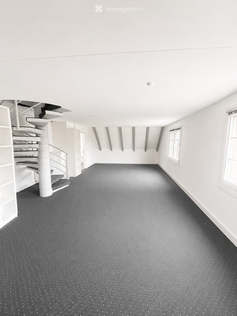Empty room with white walls, grey carpet, and a white spiral staircase leading upwards.