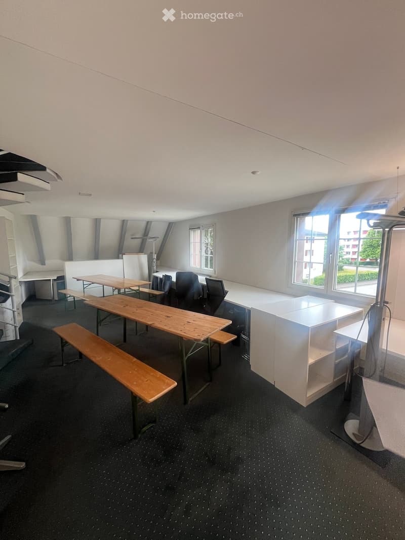 Bright room with wooden tables, benches, chairs, and white cabinets, large windows letting in natural light.