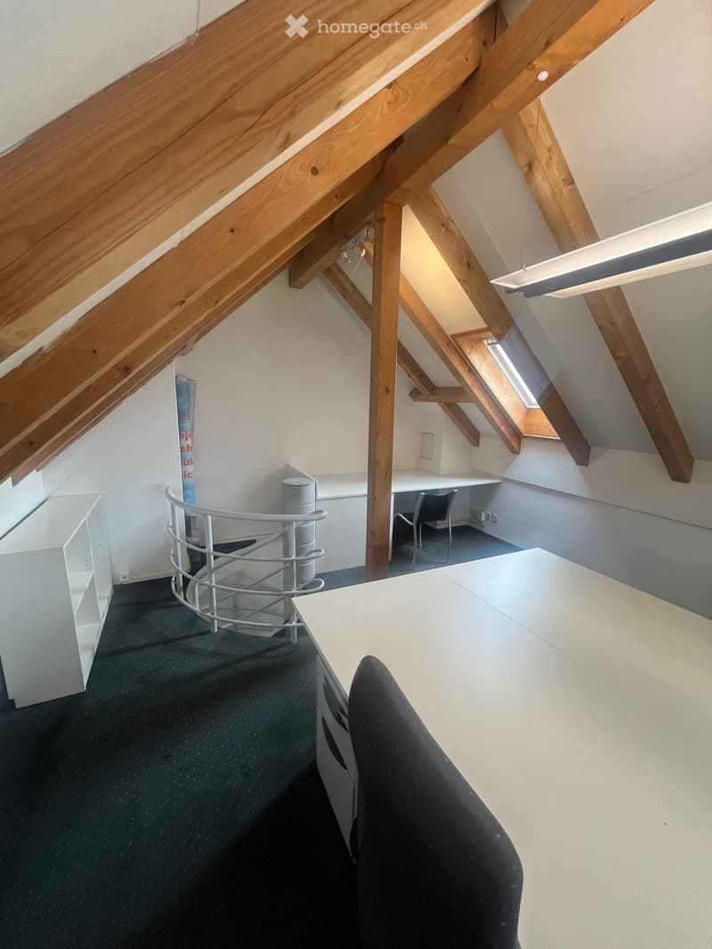 Office space with exposed wooden beams, a desk, chairs, a shelf, and a small round table with a metal frame.