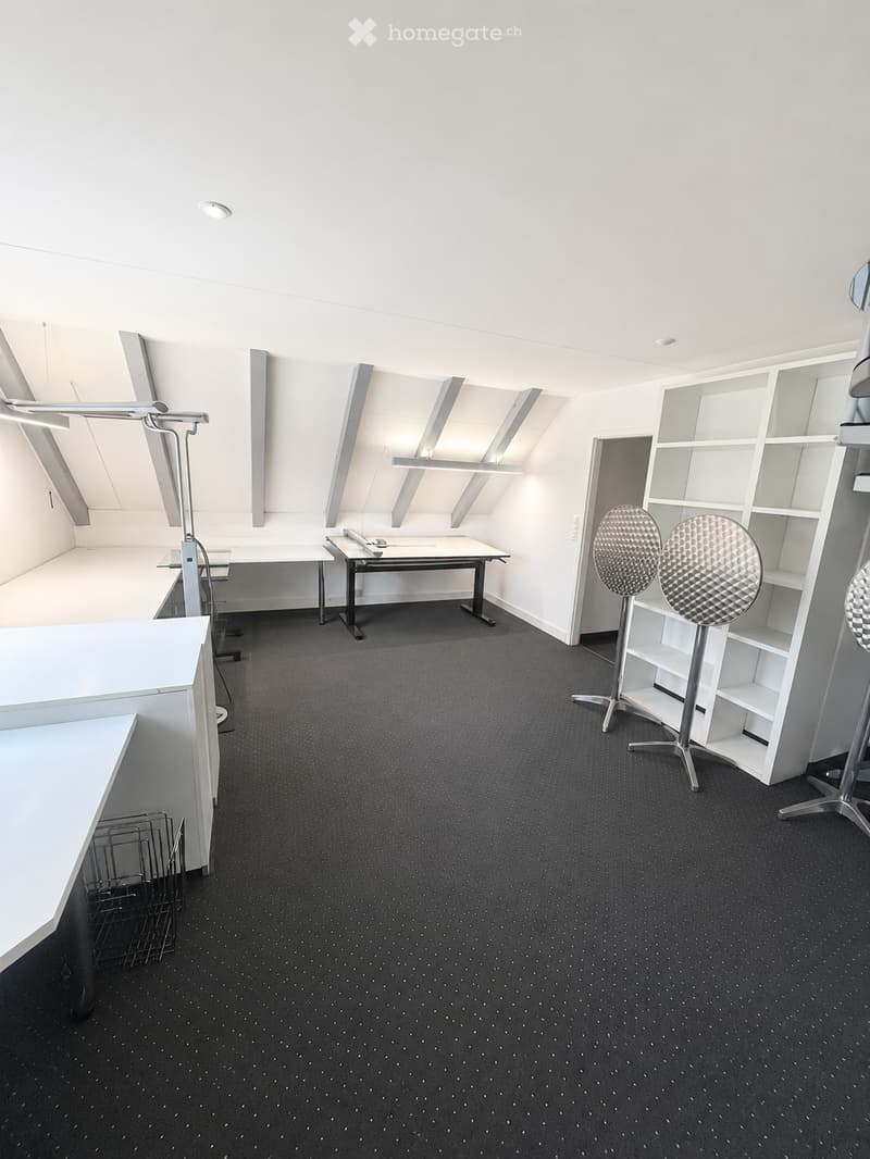 Modern, minimalist room with white walls, black carpet, and built-in shelving units. Includes a table, chairs, and stools.