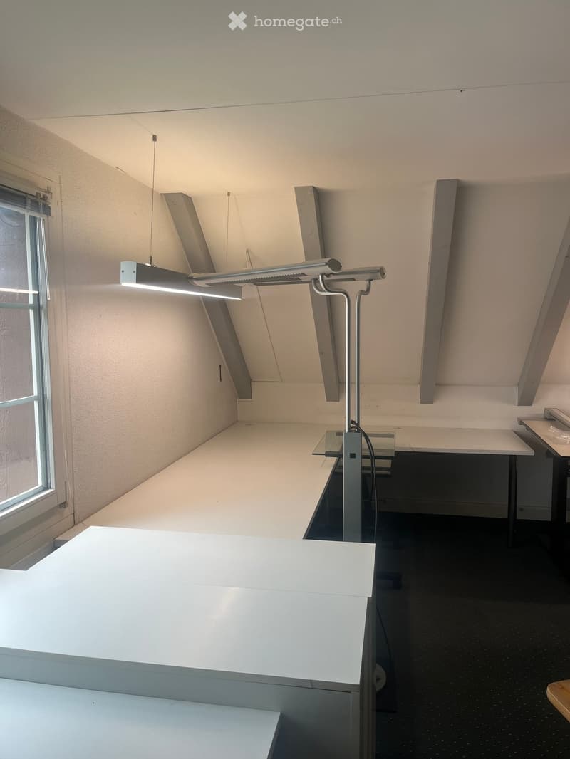 A modern, minimalist room with white tables, a sleek lamp, and a large window allowing natural light to enter.