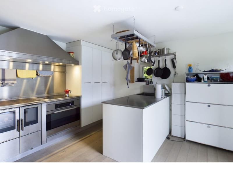 Kitchen. Modern kitchen with stainless steel appliances, white cabinets, a central island, and hanging pots and pans. Features a sleek design with ample storage and a clean, contemporary aesthetic.