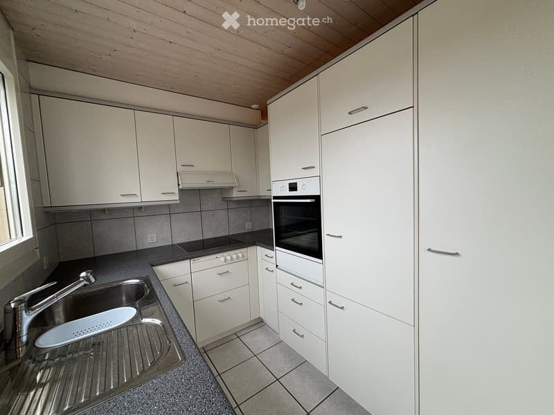 Modern kitchen with white cabinets, stainless steel sink, oven, and stove. Features a tiled backsplash and wooden ceiling.