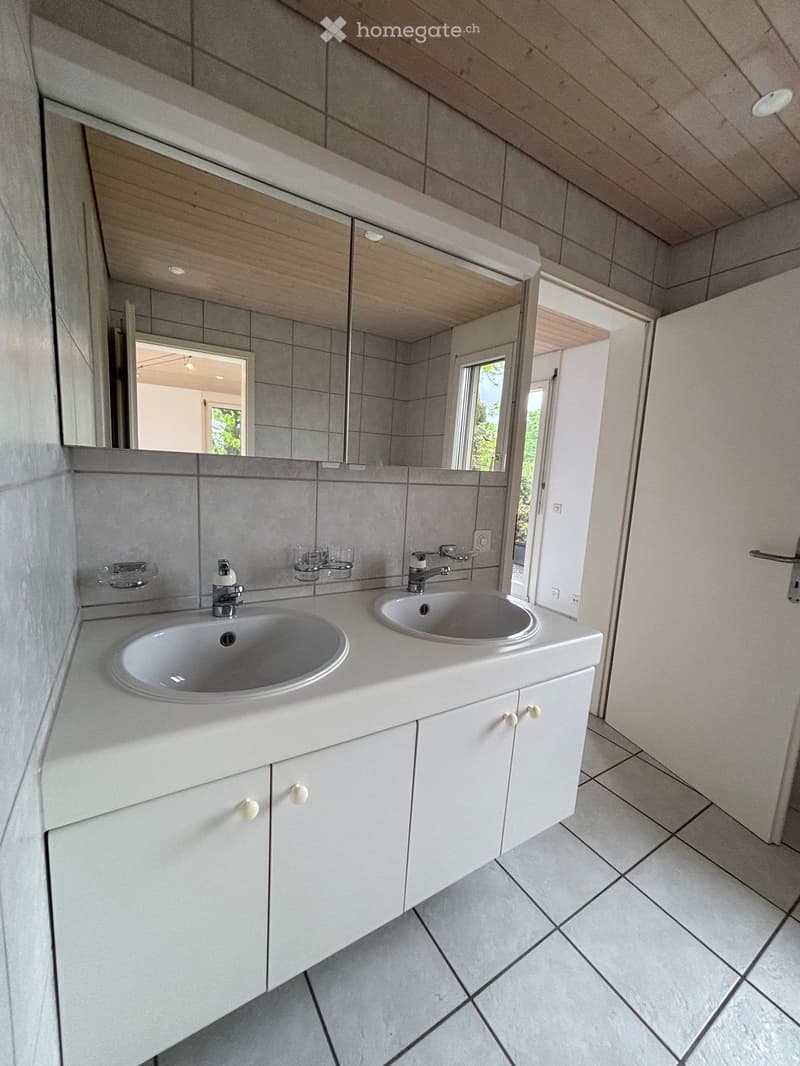 Modern bathroom with two sinks, white cabinets, and a large mirror above them. The room features tiled walls and a tiled floor.