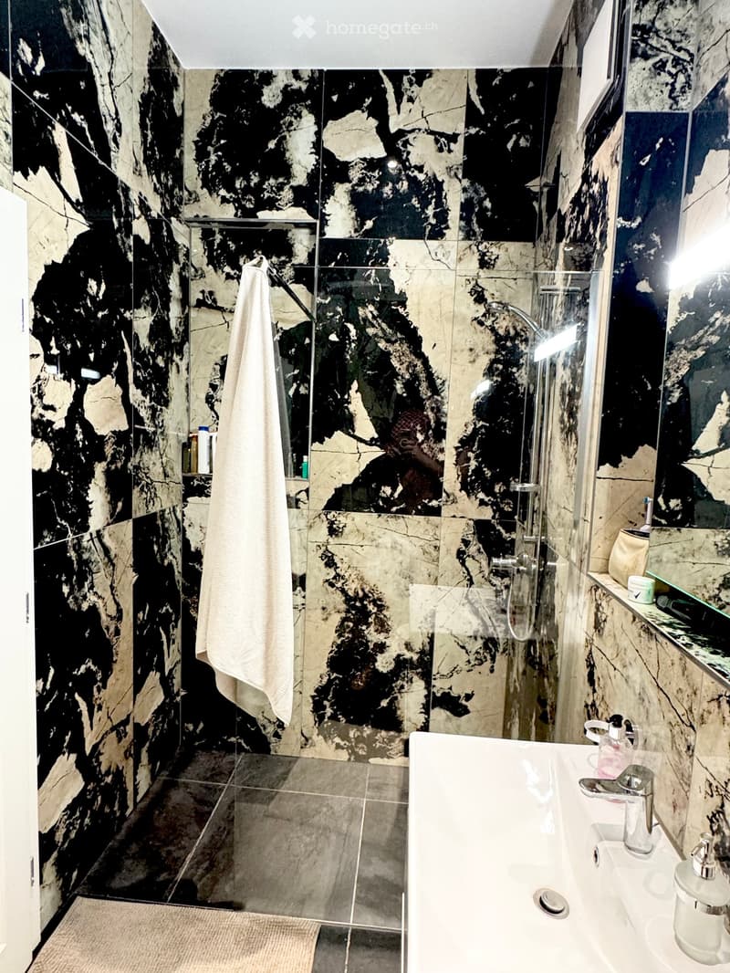 Modern bathroom with black and white marble tiles, a glass-enclosed shower, a white sink with a chrome faucet, and a towel hanging on the wall.
