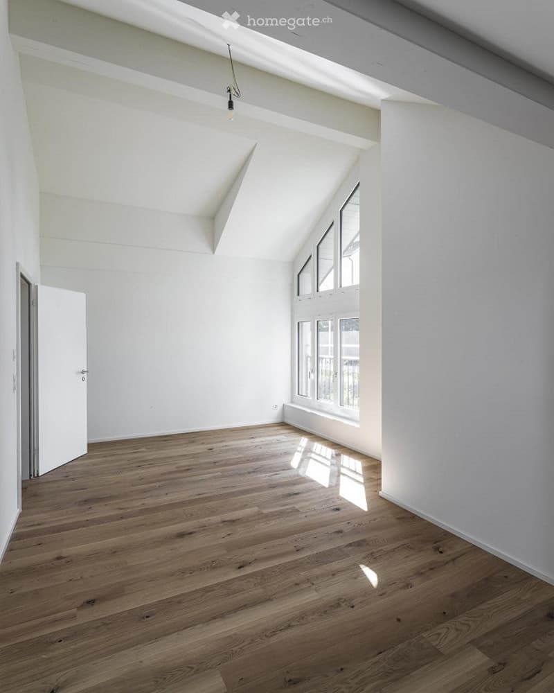 Empty room with white walls, hardwood floor, windows with balcony access, ceiling beams