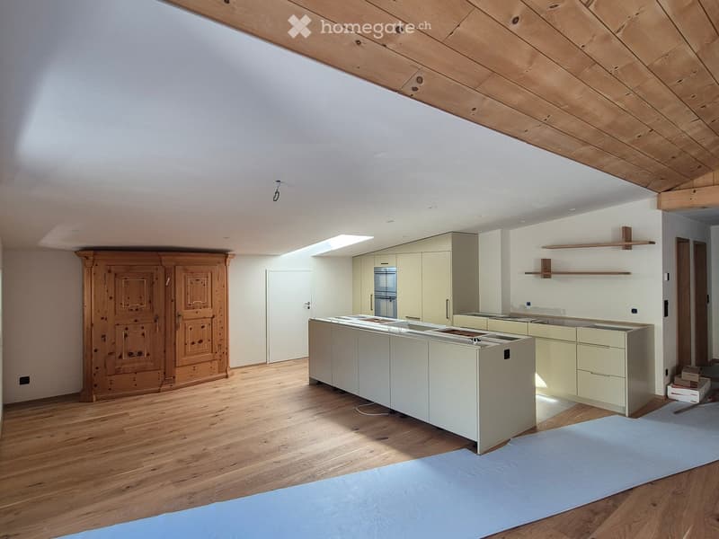 Modern kitchen with light-colored cabinets, a central island, and wooden flooring. Features include built-in storage, a large window, and exposed wooden beams on the ceiling.
