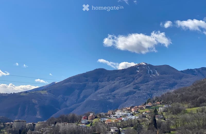 A scenic view of a town nestled in a valley surrounded by mountains under a clear blue sky.