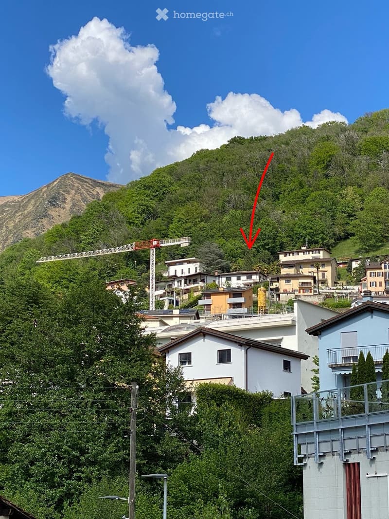 Residential area with multiple houses, surrounded by greenery and hills, with a construction crane visible in the background.