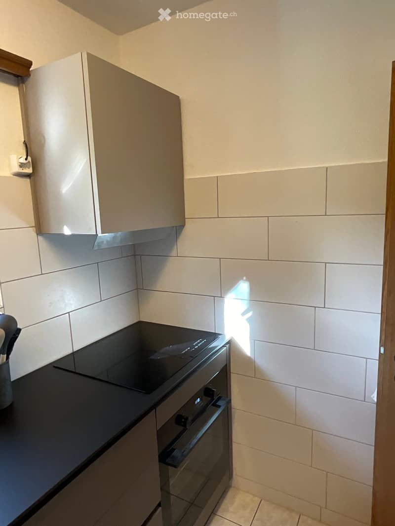 Modern kitchen with white tiled walls, black countertop, and built-in oven. Light-colored cabinets are mounted above the counter.