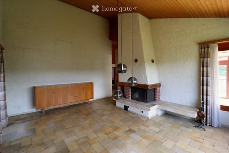 Living room with a fireplace, wooden cabinet, pendant lights, and a bench. The room features tiled flooring and large windows with curtains.