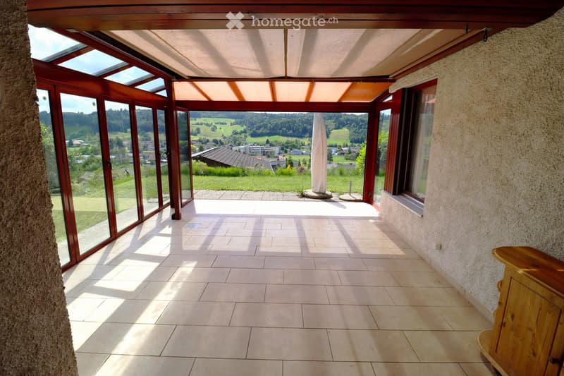 Bright sunroom with large glass windows and doors, tiled floor, and a scenic countryside view.