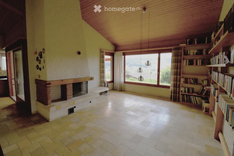 Bright living room with a brick fireplace, large windows offering a scenic view, and built-in wooden bookshelves filled with books.