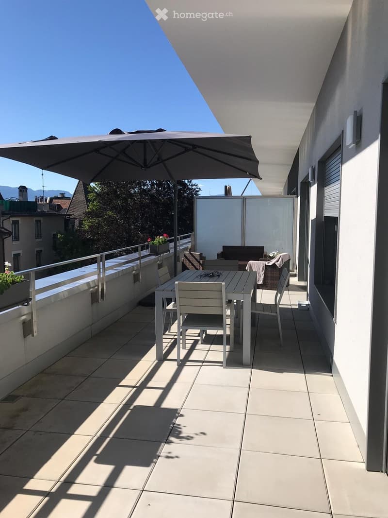 Balcony with a tiled floor, a white table and chairs, an umbrella, and a view of the city and mountains.