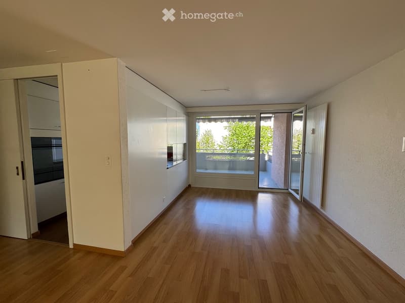 Unfurnished Room. An empty room with wooden floors, white walls, and sliding glass doors leading to a balcony. There are built-in cabinets on the left side.
