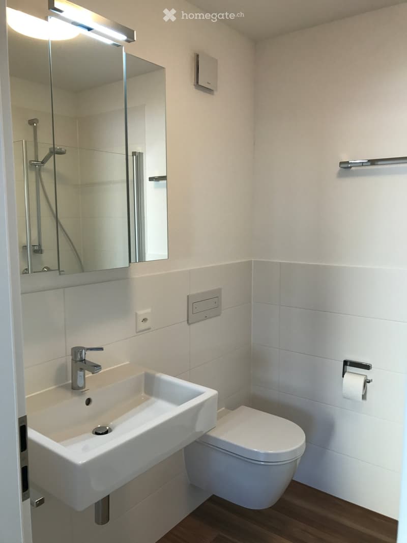 Modern bathroom with white tiles, a sink with a modern faucet, a toilet, a shower area with a glass enclosure, and a mirror above the sink.