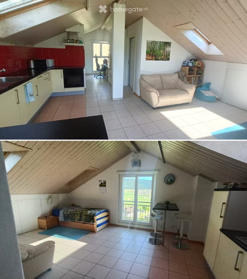 Loft-style living and sleeping area with a kitchen, sofa, bed, table, and stools. The space features exposed wooden beams and large windows with a scenic view.
