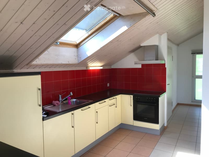 Modern kitchen with red tiled backsplash, cream-colored cabinets, stainless steel sink, and built-in oven. Features skylight windows and a sleek countertop.