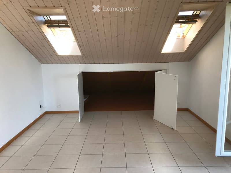Empty room with tiled floor, white walls, wooden trim, and skylights in the ceiling. No furniture or equipment present.