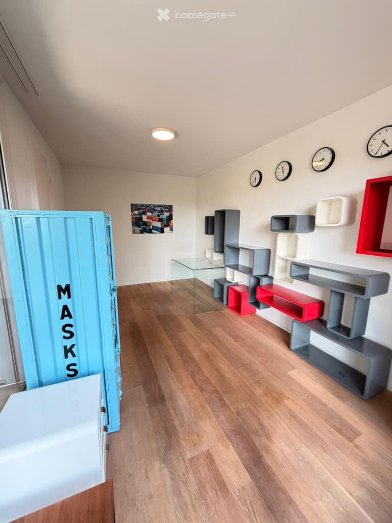 Modern, minimalist room with wooden flooring, colorful geometric shelves, a glass table, and several wall-mounted clocks.