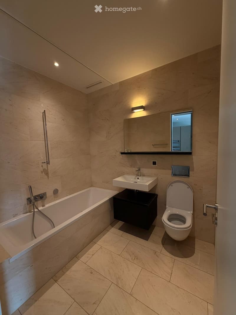 Modern bathroom with beige tiles, a bathtub, a sink with a black cabinet, a toilet, and a large mirror above the sink.