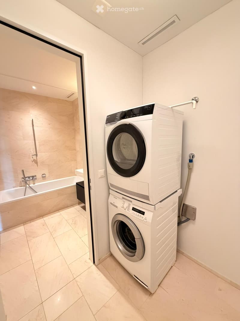 A modern bathroom with a bathtub, showerhead, and a stacked washer and dryer unit.
