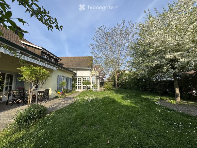 Garden / Outdoor Area. Well-maintained garden with a paved pathway, lawn, and a small seating area with a table and chairs near the house.