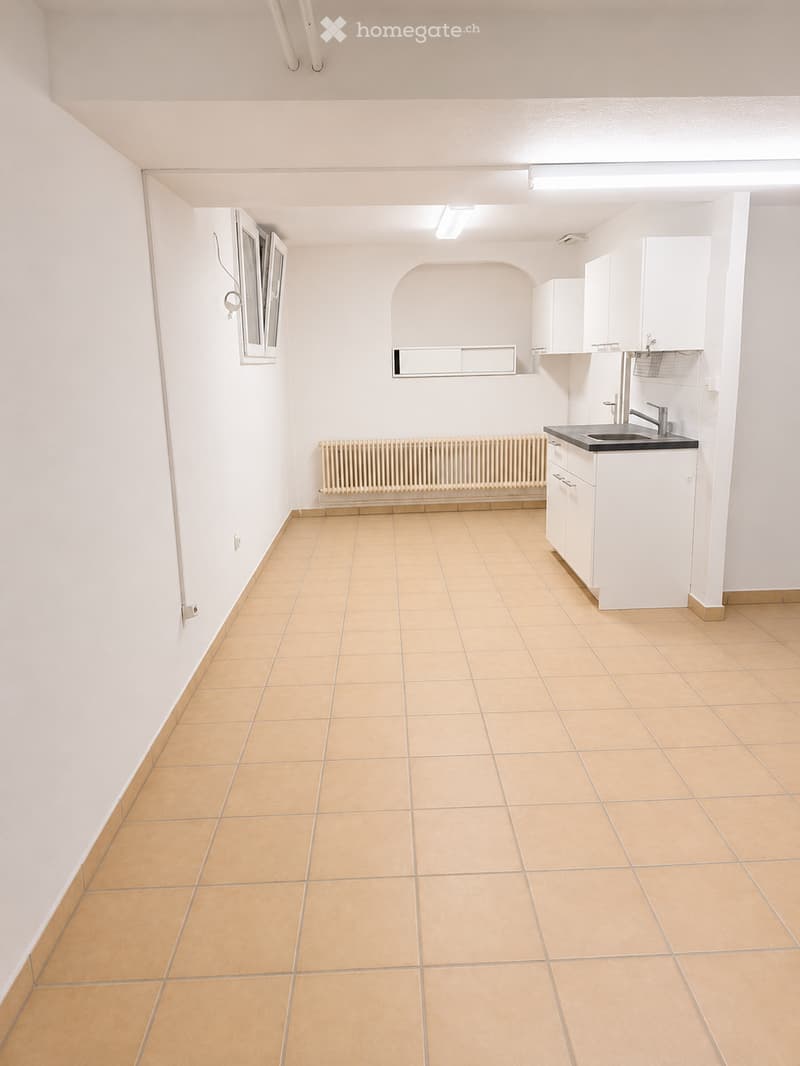 Empty kitchen with tiled floor, white cabinets, sink, and a window. No furniture or appliances are present.