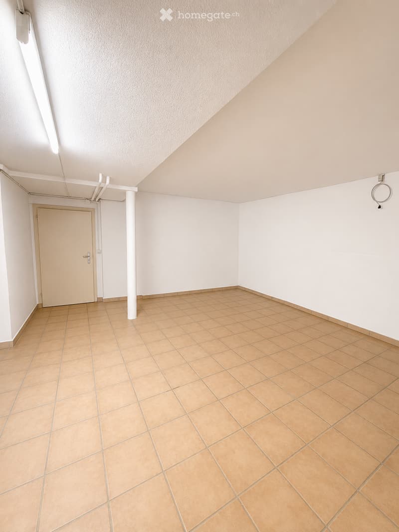 Empty room with beige tiled flooring, white walls, and a single door leading to another space. The ceiling has a textured finish and includes visible lighting fixtures.