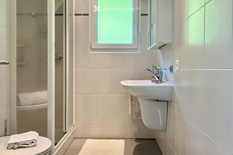white tiled walls, white floor, white toilet, white shower, white sink, white towel rack, clear shower door