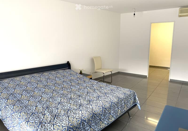 Bedroom with bed, nightstand, chair, wall decoration, tiled floor, air conditioner, and a door leading to another room.