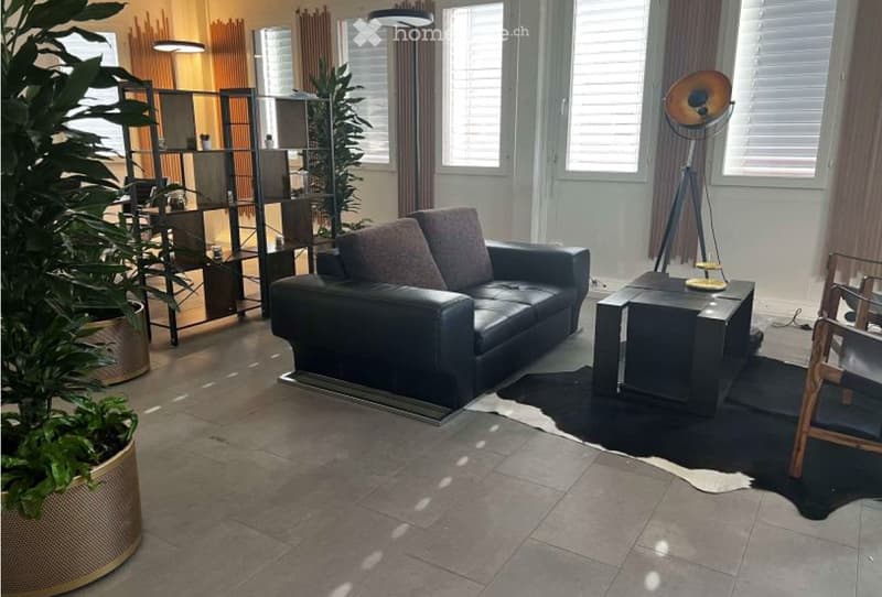 Furnished Room. Modern living room with a black leather sofa, coffee table, floor lamp, and a large potted plant. The room features large windows with blinds and a sleek, contemporary design.