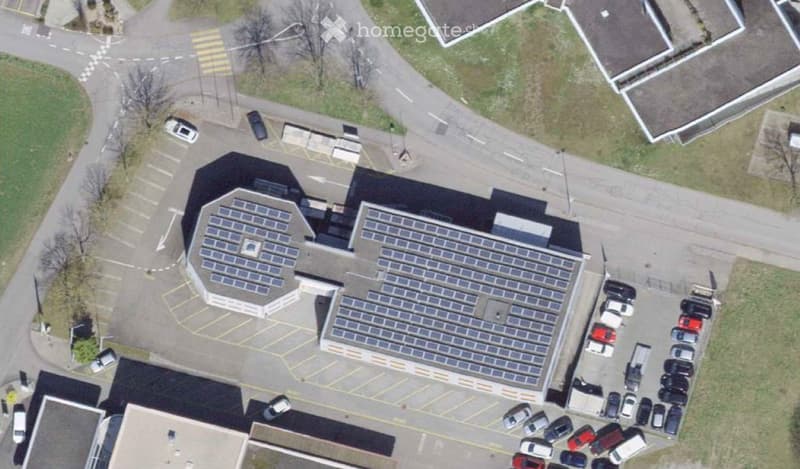 Building. Aerial view of a building with solar panels on the roof, surrounded by a parking lot with several cars.