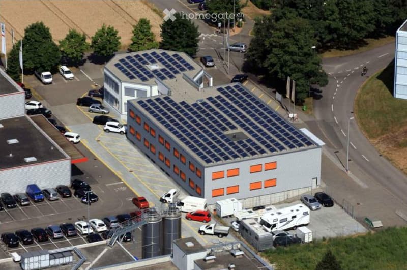 Building. Aerial view of a modern industrial building with solar panels on the roof, surrounded by a parking lot with numerous cars and a few RVs.