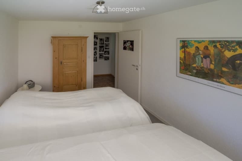 bedroom with two white double beds, wooden wardrobe, white walls, a door leading to the hallway, and a picture frame