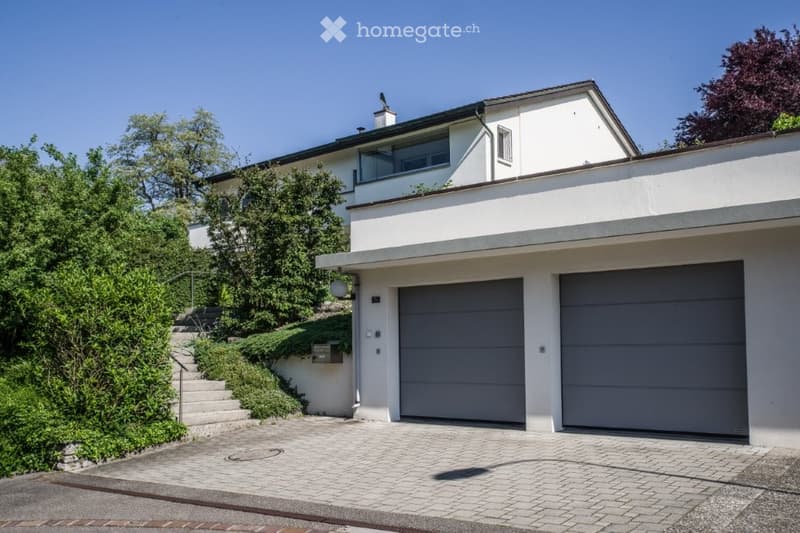 A white house with a two-car garage on a sloped driveway with a white tiled pathway.